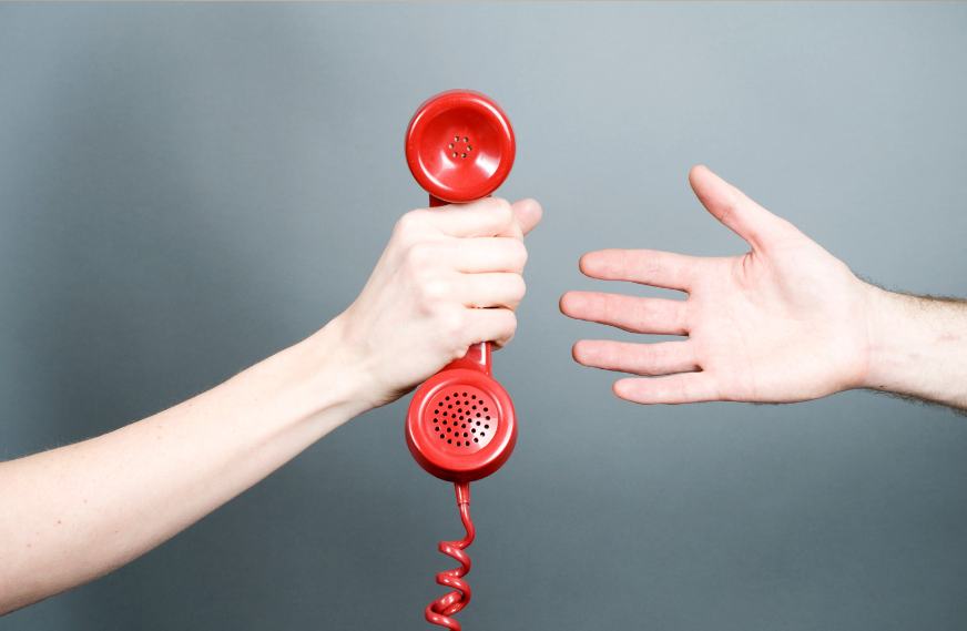 Две руки на сером фоне, одна рука держит красную трубку телефона